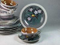 Stacked view of cups, saucers, and plates showing bird and floral design with iridescence