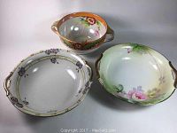 Photo showing all three Nippon porcelain bowls together including the deep iridescent glazed bowl and two berry bowls with floral decorations and handles.