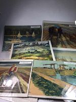 Photo showing multiple art prints laid out, each in protective sleeves with backing. Prints depict landscapes, human figures, boats, horses, and rural bridges.