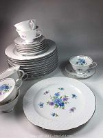 Stack of plates, cups stacked inside plates, and some cups and saucers displayed separately showing floral design and silver rims.