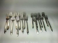 17 silver plated forks arranged on a white background, 9 larger dinner forks on left and 8 smaller salad forks on right. All forks show common wear but remain intact.