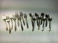 Photo showing 8 salad forks and 8 teaspoons arranged side by side with visible rose pattern handles and common wear.