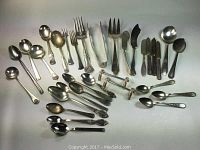 Full arrangement of assorted silverplated cutlery and serving pieces including various spoons, forks, knives, tongs, and knife rests on a white background.