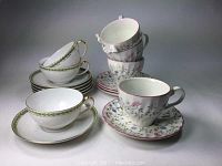 Set of porcelain teacups and saucers arranged with two groups showing different patterns and colors, photographed to show all items included in the lot.