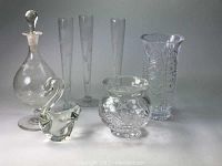 7 pieces of assorted cut and etched glassware including 3 rose etched bud vases, a swan figurine, a globe perfume or small decanter with stopper, a sawtooth cut rim vase, and a rimmed cut globe vase.