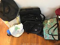 Photo showing a group of assorted bags including laptop carriers, totes, and travel bags placed on floor against wall.