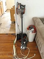 Shark Rocket vacuum cleaner standing upright with power cord coiled, next to trash can with extension cords and power strips coiled inside.