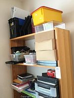 Photo showing three shelves filled with various office supplies including file storage boxes, notebooks, binders, and other items.