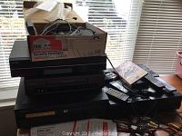 Wide view of the lot showing stacked Toshiba and Pioneer players, a box of cables, remotes, and discs.