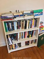 Wide view of three white shelves filled with assorted books, VHS tapes, and the Boggle game box on the top shelf
