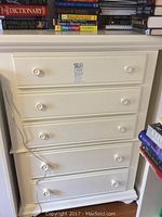 Front view of white painted Broyhill dresser with five drawers, round knob pulls, books on top
