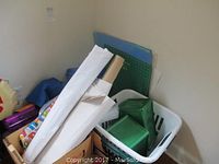 Photo showing rolls of gift wrap paper, plastic storage bins, and a cutting mat leaning against wall.