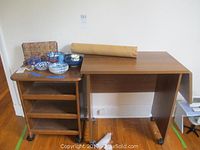 Solid wood rolling shelf with three open shelves and caster wheels next to the desk.