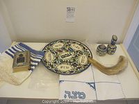 Image showing Judaica items including tallit, siddur with ornate cover, shofar, Passover plate, embroidered cloth, and ceramics
