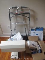 Overall view of walker, boxed scale, lamp shade, and boxes containing items on floor