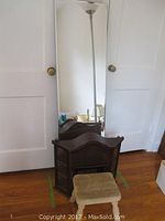 Mirror, curio cabinet, and wood foot stool placed against white door on wooden floor