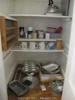 Shelf inside a cupboard showing coffee mugs, kitchen containers, metal bakeware including pans and trays.