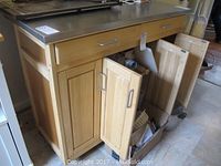 Front view of the wooden kitchen island with stainless steel countertop showing open cabinet doors and drawer.