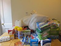 Photo showing assorted kitchen cleaning and storage supplies on a table including paper towels, wipes, several boxes of Ziploc bags and garbage bags, Swiffer and Cascade products.