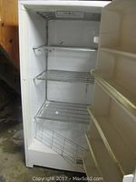 Open GE standing freezer in basement showing interior wire shelves and door storage.