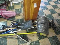 View of snow shovel, garden shovel, metal rake, and manual hand mowers on floor.