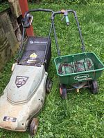 Both items together outside on grass, lawn mower and seed spreader visible with dirt and rust.