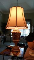 Lamp fully assembled with lit fabric shade, showing scalloped edge and height proportion in a living room setting.