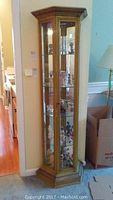 Full view of gold tone corner curio cabinet showing shape, glass doors and shelves with items displayed inside.