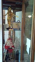 Curio cabinet glass shelves containing Egyptian statues, crystal bells, doll and metal salt cellars.