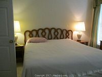 Full view of king bed from the foot, showing wooden headboard with curved design, white bedding, bedside tables with lamps.