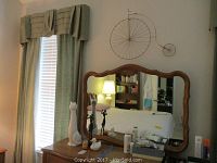Metal vintage penny-farthing bicycle wall art mounted on wall above mirror in bedroom setting, showing detail and placement.