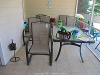 Six mesh and metal patio chairs with arms arranged on tiled porch beside a glass patio table with black metal frame.
