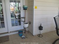 4-tier metal plant stand with four ceramic planters in white and blue, positioned in a corner on tiled flooring near a glass door.