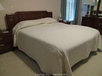 Full view of bed made up with white quilted comforter in bedroom setting, showing bed size and condition.