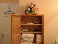 Bathroom shelf with neatly folded white towels and washcloths, hair dryer, curling iron, floral arrangement, decorative soaps in a small glass and brass octagon box.