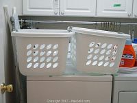 Two white Sterlite laundry baskets with oval ventilation holes on top of a white appliance in a laundry room.