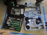 Open molded plastic Alltrade tool and socket case with green-handled tools, sockets, pliers, and screwdrivers visible. Gray molded plastic Dremel case open showing cordless rotary tool cordless tool, charger, and accessories inside.