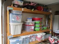 Photo of wooden shelving unit with stacked storage boxes and containers holding seasonal decorations including wreaths and assorted decor items.