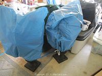 Two faux poinsettia plants covered in blue protective bags on black ceramic urn bases.