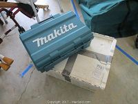 Closed Makita branded blue hard plastic carrying case on top of a white box in garage environment.