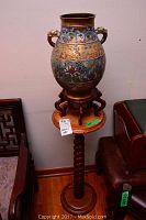 Full view of cloisonné vase atop small stand on tall pedestal