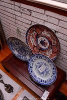 Three plates displayed on wooden stands against a white brick wall