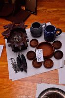Full lot showing cuckoo clock, two beer mugs, large wooden bowl surrounded by seven smaller wooden bowls on paper on hardwood floor.