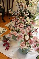 Wide shot showing all three decorative artificial flower plants on display with pink and purple flowers and green leaves in light blue-green ceramic vases.