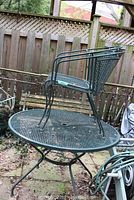Outdoor metal mesh table with one chair on top and one chair beside it, showing condition and size.