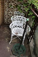 Pair of white metal outdoor chairs with ornate scrollwork along with a black metal umbrella base showing some wear and use on a patio floor.