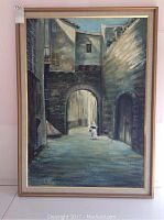 Frontal photo of original Orihuela oil painting showing a realistic architectural street scene with archway and figure. Painting framed in gold frame, frame shows wear.