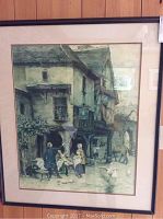 Full view of framed artwork depicting a village scene, black wooden frame with cream mat against wood panel background