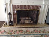 Fireplace showing iron fireplace tools on stand, iron pitchfork, brass trimmed fireplace screen, and decorative hearth border.
