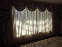 Full span of wall showing heavy drapes with scalloped swags and sheer panels behind, on carpeted floor.